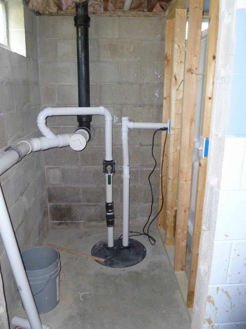 Professional sewage ejector pump installation with basin and discharge piping for basement bathroom